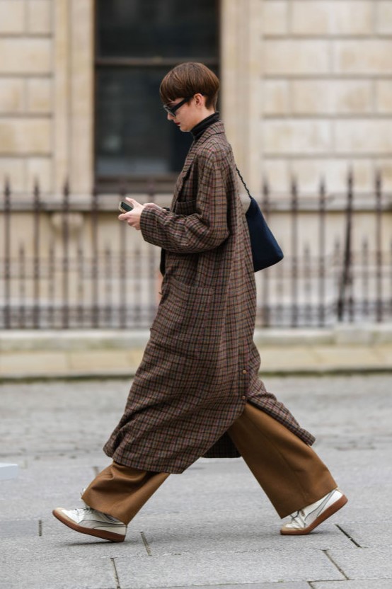 LONDON, ENGLAND - FEBRUARY 20: A model wears black sunglasses, a black turtleneck pullover, a brown and red checkered print pattern wool long coat, a black shoulder bag, a black shiny leather belt, grown suit pants, beige sneakers , outside Emilia Wickstead, during London Fashion Week February 2023 on February 20, 2023 in London, England. (Photo by Edward Berthelot/Getty Images)