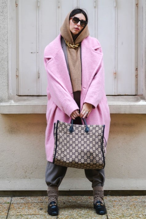 PARIS, FRANCE - JANUARY 13: Gabriella Berdugo wears Fendi sunglasses, a golden large chain necklace from Brinker and Eliza, a pink oversized long wool coat from Essentiel, a taupe boyish suit and blazer jacket from In Wear, a brown wool knitted hoodie sweater / pullover from Zara, black leather loafer shoes from Gucci, brown wool socks over the pants, a brown wool monogram printed tote bag from Gucci, on January 13, 2021 in Paris, France. (Photo by Edward Berthelot/Getty Images)