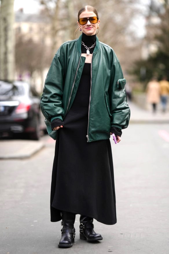 PARIS, FRANCE - MARCH 07: Marianne Theodorsen wears black and orange sunglasses, a black turtleneck / cut-out chest / long dress, a dark green shiny leather oversized bomber coat from Prada, black shiny leather belted knees boots / high boots , outside Awake, during Paris Fashion Week - Womenswear Fall Winter 2023 2024, on March 07, 2023 in Paris, France. (Photo by Edward Berthelot/Getty Images)