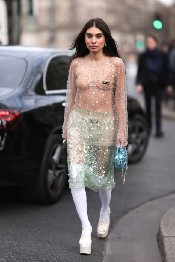 PARIS, FRANCE - MARCH 07: Fer Millan Delaroiere seen wearing a transparent glitter sequins dress with a blue shiny bag, white socks and white plateau heels before the Miu Miu show on March 07, 2023 in Paris, France. (Photo by Jeremy Moeller/Getty Images)