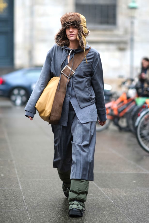 COPENHAGEN, DENMARK - JANUARY 30: A guest wears a brown fluffy chapka hat, a blue jacket, a beige leather large oversized crossbody bag, a pleated skirt, rainproof boots, outside Aeron, during the Copenhagen Fashion Week AW24 on January 30, 2024 in Copenhagen, Denmark. 