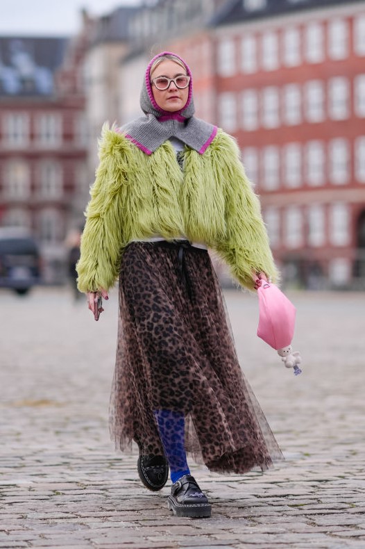 COPENHAGEN, DENMARK - JANUARY 31: A guest wears a purple and gray ribbed wool balaclava / hood, a yellow / green fluffy oversized jacket , a flowing tulle leopard print pattern gathered and pleated skirt, blue tights, black leather shoes, a pink bag outside Wood Wood, during the Copenhagen Fashion Week AW24 on January 31, 2024 in Copenhagen, Denmark.