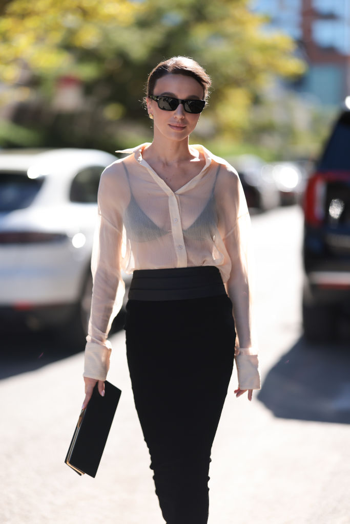 NEW YORK, NEW YORK - SEPTEMBER 08: Mary Leest is seen wearing rectangular black sunglasses from Persol, gold round structured earrings, a transparent beige long-sleeved blouse tucked into a fitted black maxi skirt, a black bra underneath, and a rectangular black leather clutch before the Ulla Johnson Show during New York Fashion Week on September 08, 2024, in New York City. (Photo by Jeremy Moeller/Getty Images)