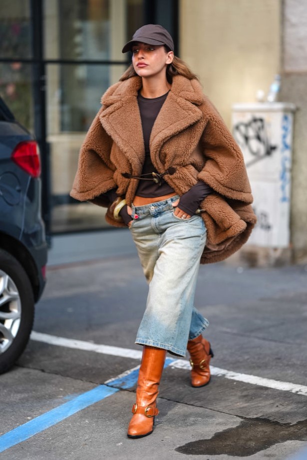 MILAN, ITALY - SEPTEMBER 19: A guest wears dark brown Baseball hat, dark brown long sleeve shirt, light brown teddy bear oversized Max Mara coat, washed denim jean jorts, light brown heeled leather boots, outside Max Mara, during the Milan Fashion Week Spring/Summer 2024-2025 on September 19, 2024 in Milan, Italy. (Photo by Edward Berthelot/Getty Images)