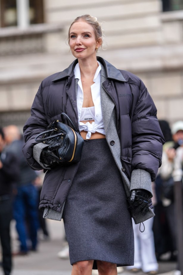 PARIS, FRANCE - OCTOBER 01: Leonie Hanne wears white Miu Miu bralette, white buttoned up long sleeve tied shirt, dark gray Miu Miu blazer jacket, black high waisted Miu Miu over the knee skirt, shiny black quilted puffer jacket, shiny black Miu MIu leather bag, outside Miu Miu, during the Paris Fashion Week Spring/Summer 2025 on October 1, 2024 in Paris, France